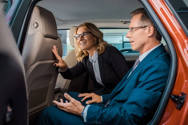 Vista laterale di uomini d'affari seduti sul retro sedersi in auto nuova nel salone di concessionaria — Foto stock