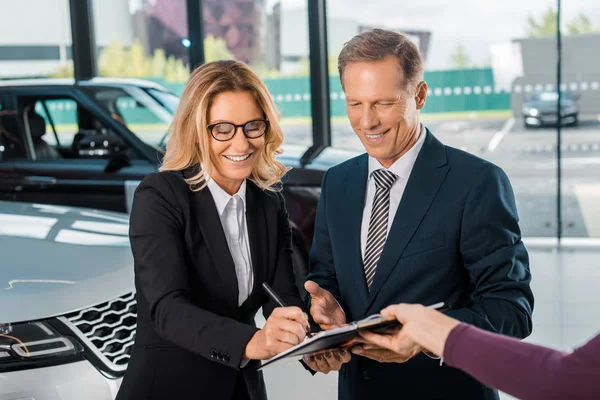 Feliz pareja de negocios firmando papeles para comprar un coche nuevo en la sala de exposición - foto de stock