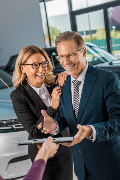 Glückliches Geschäftspaar unterschreibt Papiere für den Kauf eines neuen Autos im Showroom — Stockfoto