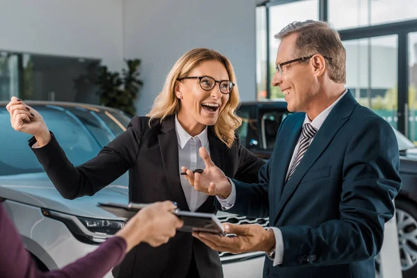 Happy businesspeople and female car dealer with documents in showroom — Stock Photo