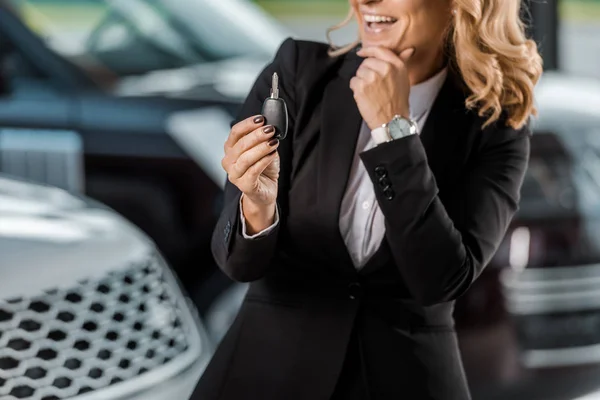Обрезанный снимок улыбающейся деловой женщины, держащей ключ от машины в выставочном зале — стоковое фото