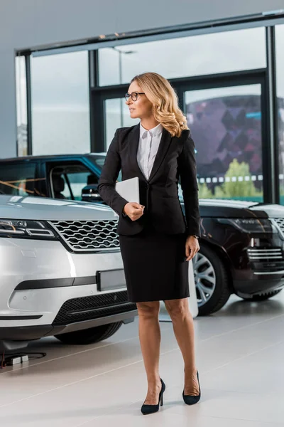 Hermosa concesionaria de coches femeninos con tableta caminando por sala de exposición - foto de stock