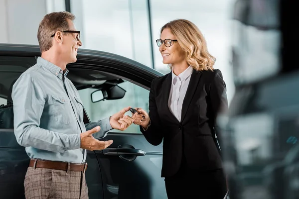 Adult man taking car key from female car dealer at showroom — Stock Photo