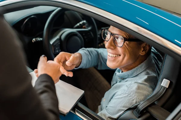 Cropped shot of female car dealer passing car dealership contract to smiling adult man in showroom — Stock Photo