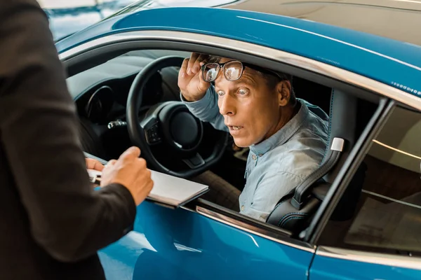 Ritagliato colpo di concessionario auto femminile che mostra contratto di concessionaria auto per uomo scioccato nello showroom — Foto stock