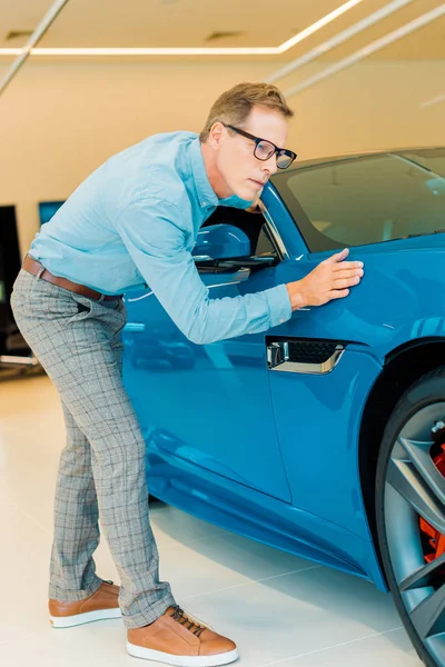 Atractivo hombre adulto tocando coche deportivo de lujo en el showroom - foto de stock