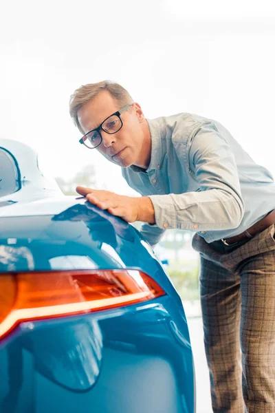 Handsome adult man touching luxury sport car at showroom — Stock Photo