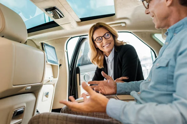 Close-up shot of adult man and female car dealer sitting on back seat of luxury car and talking — Stock Photo