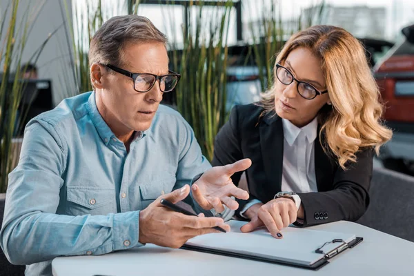 Adult man and female car dealer discussing contract at showroom — Stock Photo