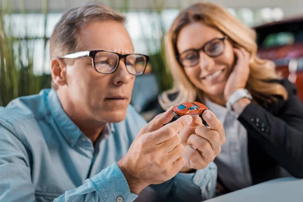 Close-up shot of adult man and female car dealer looking at toy car in showroom — Stock Photo