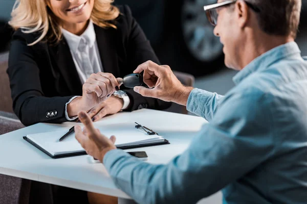 Cropped shot of adult customer and female car dealer passing car key in showroom — Stock Photo