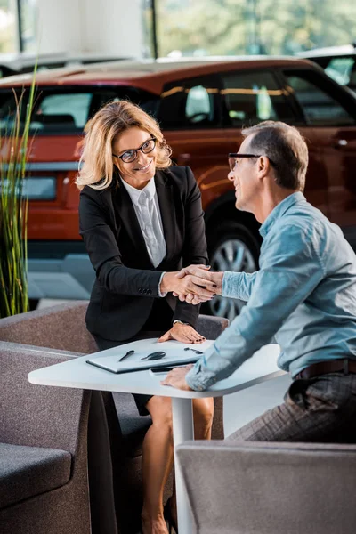 Adult customer and female car dealer shaking hands in showroom — Stock Photo