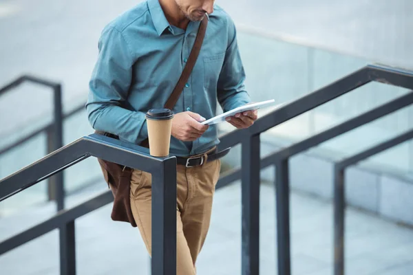 Tiro cortado do homem usando tablet digital enquanto estava em pé sobre escadas com café para ir sobre trilhos — Fotografia de Stock