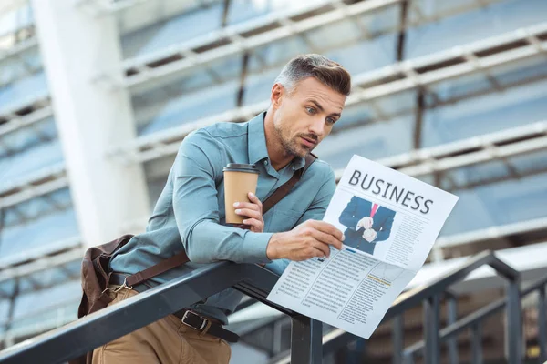 Sorprendido hombre de mediana edad sosteniendo café para ir a leer el periódico de negocios - foto de stock