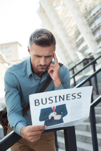 Focused middle aged man leaning at railing and reading business newspaper — Stock Photo