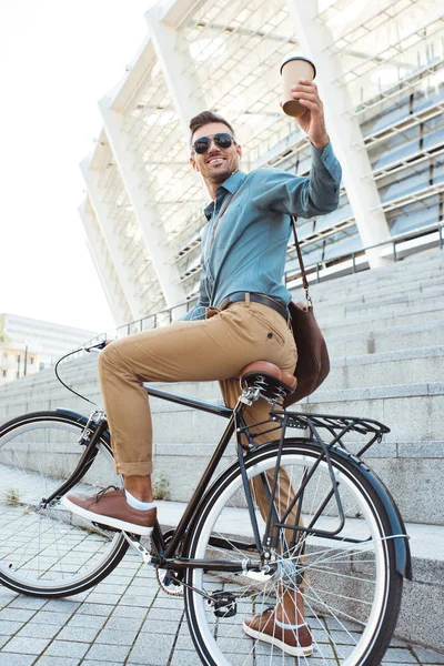 Vue à angle bas d'un homme souriant assis sur un vélo et tenant une tasse de café jetable — Photo de stock