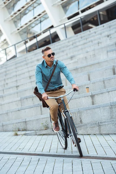 Стильный мужчина средних лет в солнечных очках на велосипеде по улице — стоковое фото