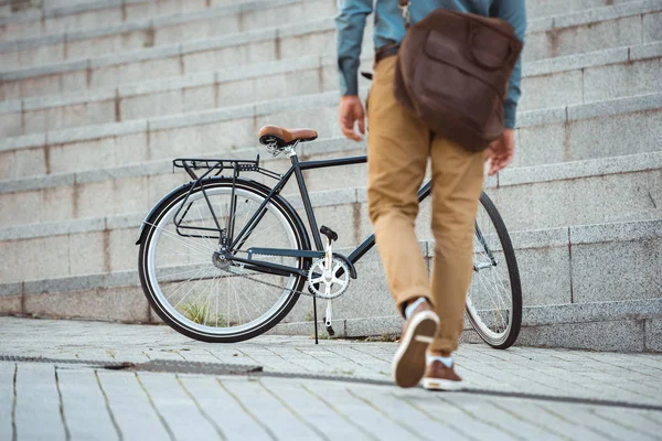 Low section of man with leather bag walking to bicycle on street — Stock Photo