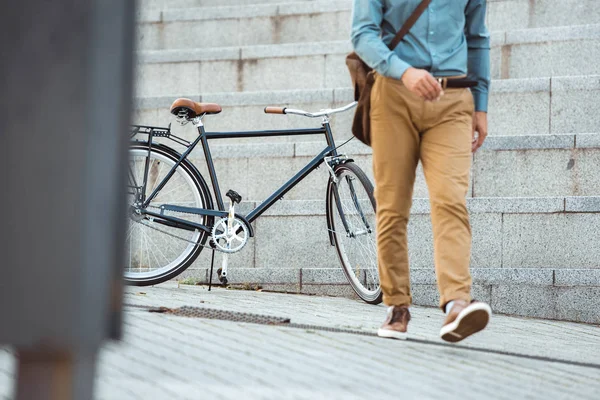 Seção baixa de homem elegante andando na rua, bicicleta estacionada atrás — Fotografia de Stock