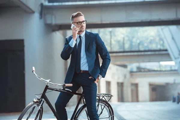 Schöner Geschäftsmann sitzt auf dem Fahrrad und spricht mit dem Smartphone auf der Straße — Stockfoto