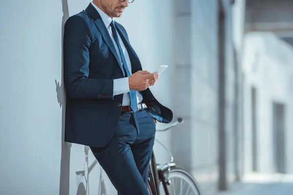 Cropped shot of businessman leaning at wall and using smartphone — Stock Photo