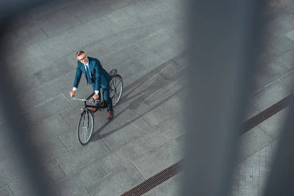 Високий кут зору красивого бізнесмена середнього віку в костюмі та окулярах їзда на велосипеді — стокове фото