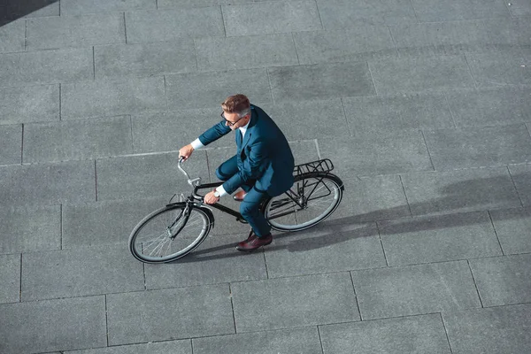 Високий кут зору середнього віку бізнесмен в костюмі і окулярах їзда на велосипеді на вулиці — стокове фото