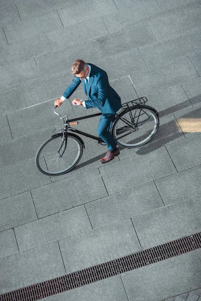 Vue grand angle de l'homme d'affaires dans l'usure formelle vélo d'équitation et de vérifier la montre-bracelet — Photo de stock