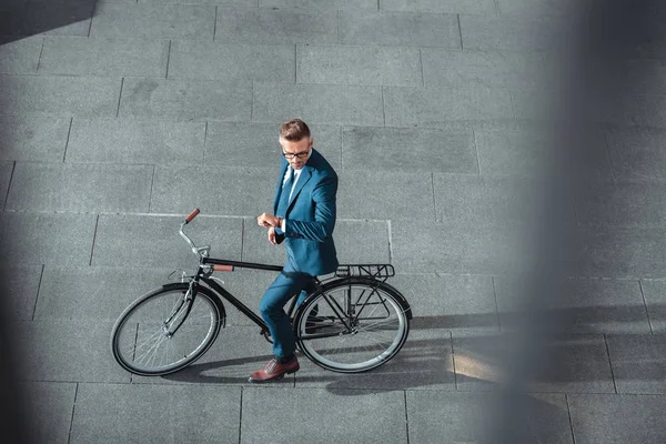 Високий кут зору бізнесмена в офіційному одязі сидить на велосипеді і перевіряє наручний годинник — стокове фото
