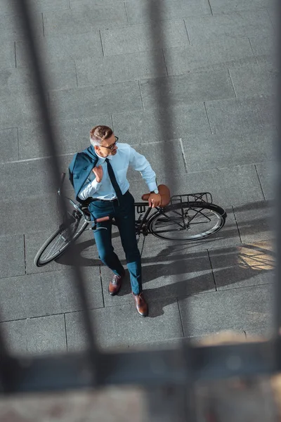 Vista de ángulo alto de hombre de negocios de mediana edad sosteniendo chaqueta de traje y mirando hacia otro lado mientras está sentado en bicicleta - foto de stock