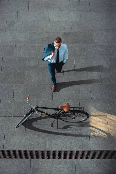 Vista ad alto angolo di uomo d'affari che tiene giacca tuta e guardando la bicicletta sulla strada — Foto stock