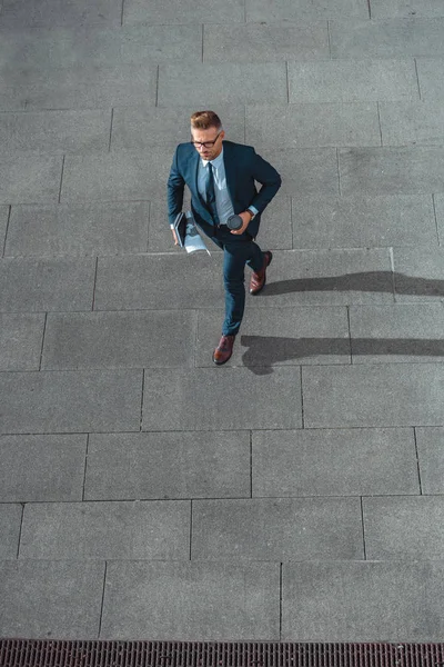 High angle view of businessman with paper cup and newspaper walking on street — Stock Photo