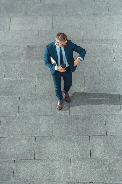 Vue grand angle de succès homme d'affaires d'âge moyen tenant café pour aller vérifier la montre-bracelet sur la rue — Photo de stock