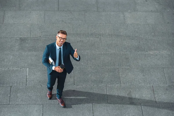 High angle view of happy businessman holding paper cup and showing thumb up on street — Stock Photo