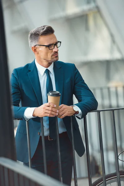 Sérieux homme d'affaires d'âge moyen dans les lunettes tenant tasse en papier et détournant les yeux — Photo de stock