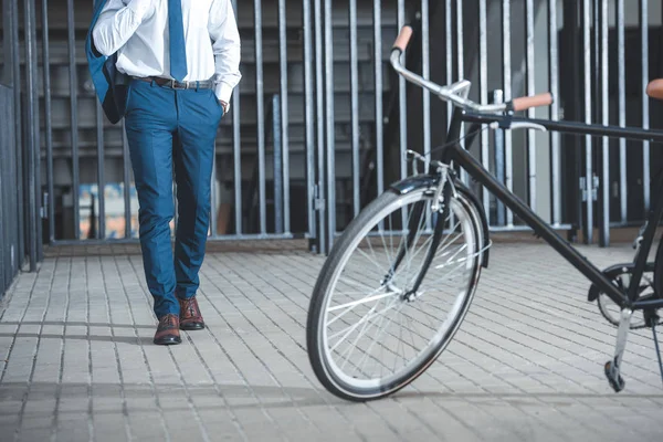 Bicicleta estacionada na rua e seção baixa do homem de negócios andando atrás — Fotografia de Stock