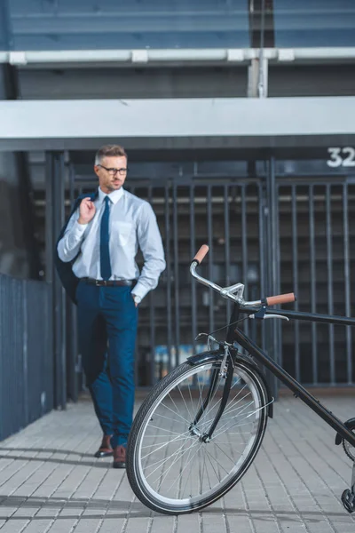 Bicicleta na rua e homem de negócios de meia idade em pé atrás — Fotografia de Stock