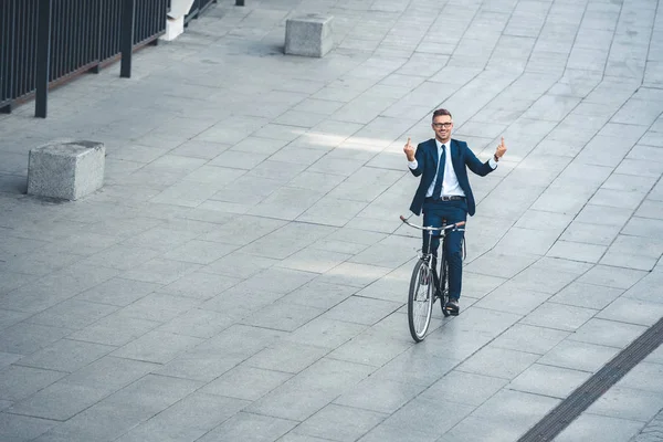 Високий кут зору середнього віку бізнесмен показує середні пальці і посміхається на камеру під час їзди на велосипеді на вулиці — стокове фото