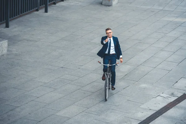 Високий кут зору щасливого бізнесмена середнього віку, що показує великий палець вгору і посміхається на камеру під час їзди на велосипеді на вулиці — стокове фото