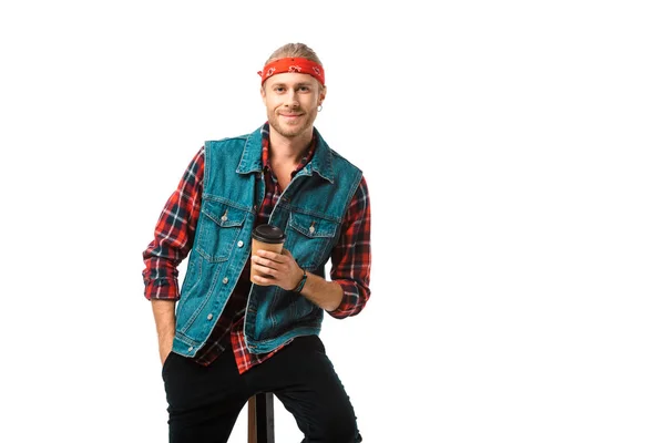 Smiling man in headband and denim vest sitting on chair with coffee cup isolated on white — Stock Photo