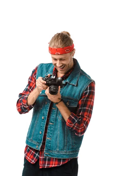 Sorrindo hipster fotógrafo masculino em colete jeans e camisa quadriculada olhando para a tela da câmera isolada no branco — Fotografia de Stock