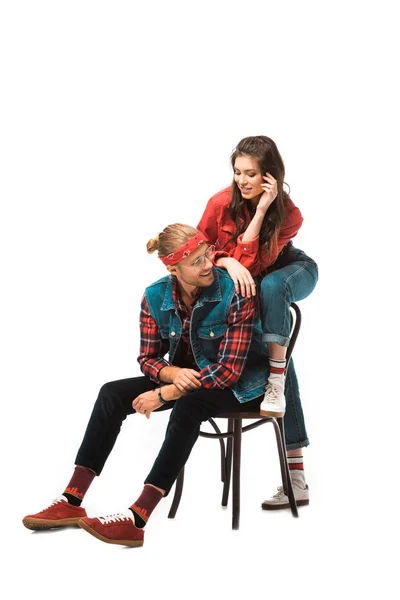 Alegre joven sentado en silla mientras su hipster chica de pie detrás aislado en blanco - foto de stock