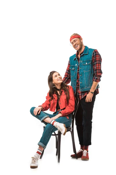 Attractive hipster girl sitting on chair while her smiling boyfriend standing behind isolated on white — Stock Photo