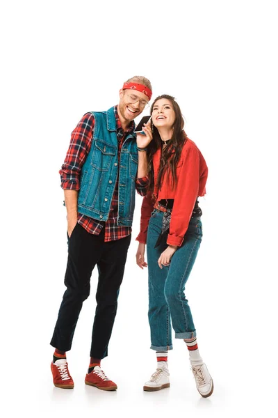Feliz jovem hipster falando no smartphone enquanto sua namorada de pé perto isolado no branco — Fotografia de Stock