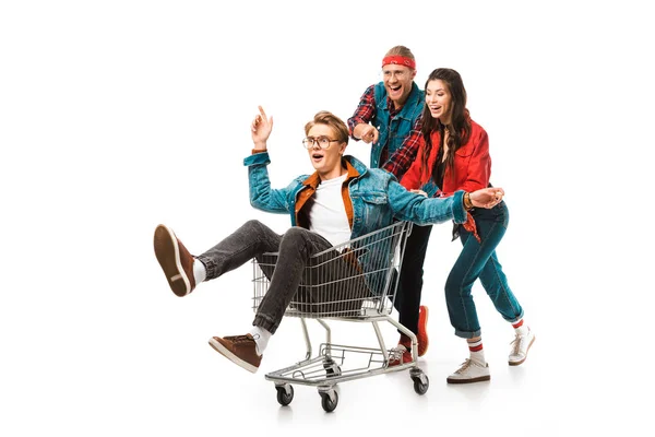 Laughing stylish hipsters having fun with shopping cart isolated on white — Stock Photo