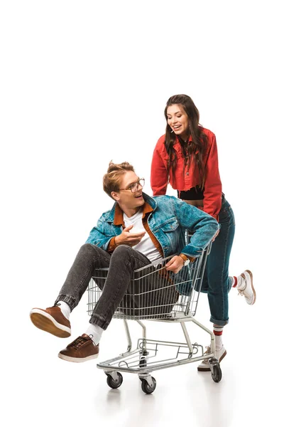 Attraktives Hipster-Mädchen trägt Einkaufswagen mit lächelndem Freund isoliert auf Weiß — Stockfoto