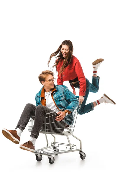 Aufgeregtes Hipster-Mädchen springt und trägt Einkaufswagen mit Freund isoliert auf weißem Grund — Stockfoto