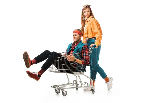 Hipster ragazza che trasporta carrello della spesa con fidanzato isolato su bianco — Foto stock