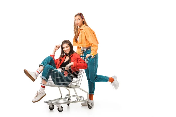 Niñas hipster feliz divertirse con carrito de compras aislado en blanco - foto de stock