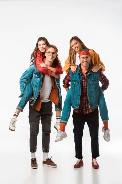 Happy stylish hipsters doing piggyback ride to their smiling girlfriends isolated on white — Stock Photo